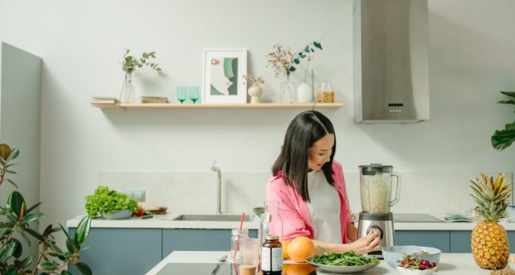 A woman blends fresh ingredients for a healthy smoothie in a stylish kitchen, promoting wellness.