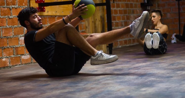 A man and woman perform core exercises with a medicine ball in a brick wall gym.